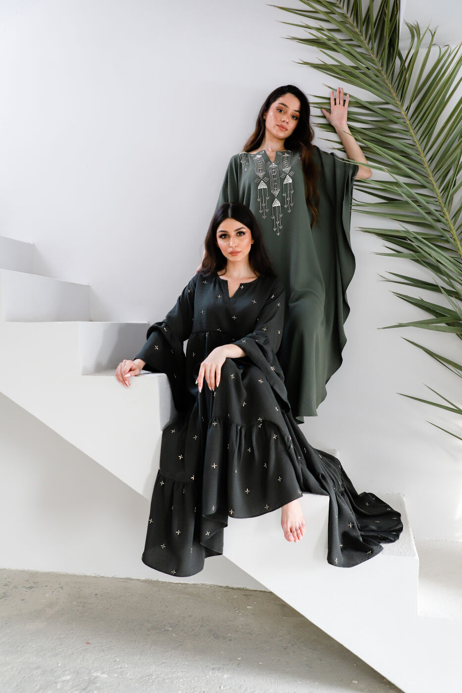 Two models in olive green embroidered kaftans on a staircase