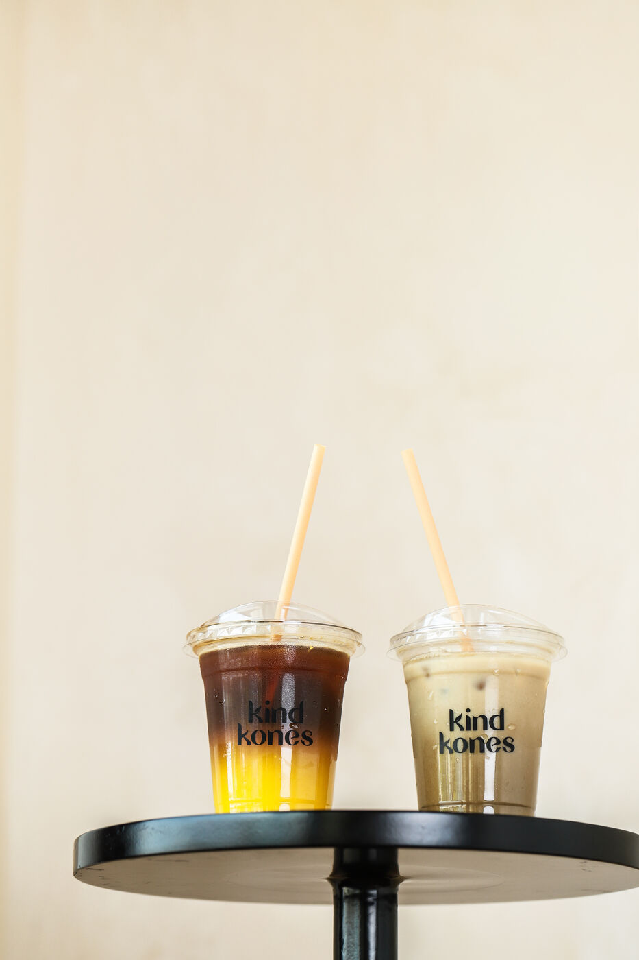 Two Kind Kones iced drinks with straws on a black side table