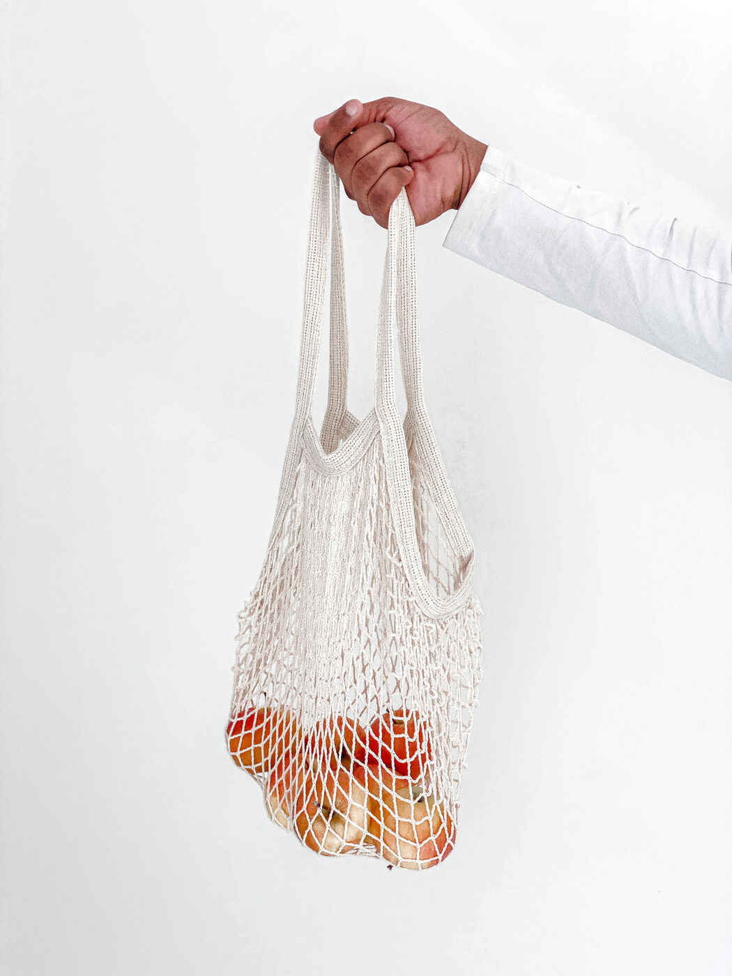Hand holding a cotton mesh grocery bag of fruit