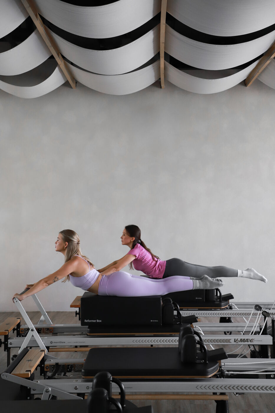 Two women in matching poses on pilates reformer machines