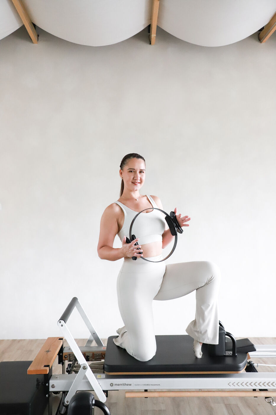 Woman kneeling on a pilates reformer holding a pilates ring
